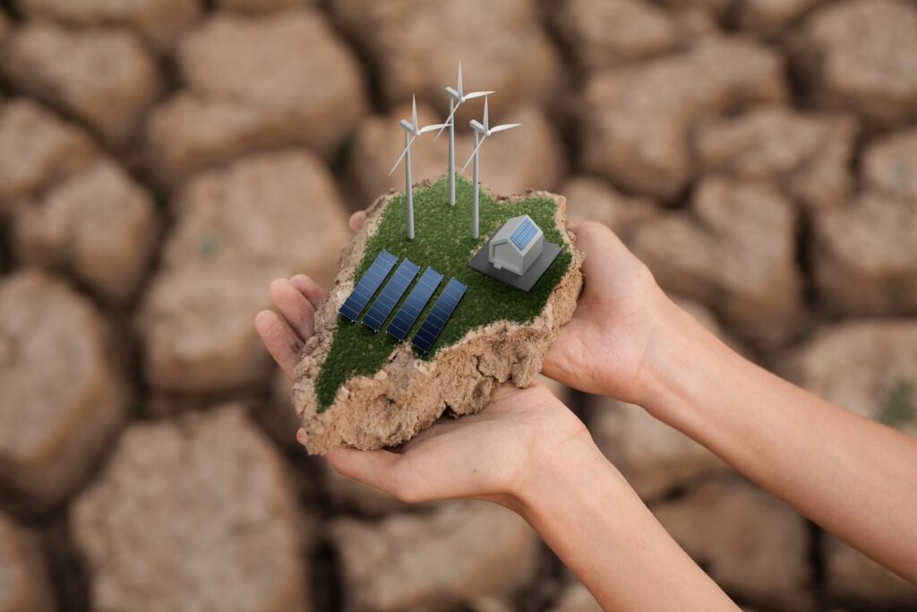 岩が背景。両手の上に大地が乗っている。大地には太陽光パネルと風力発電、家が乗っている。画像