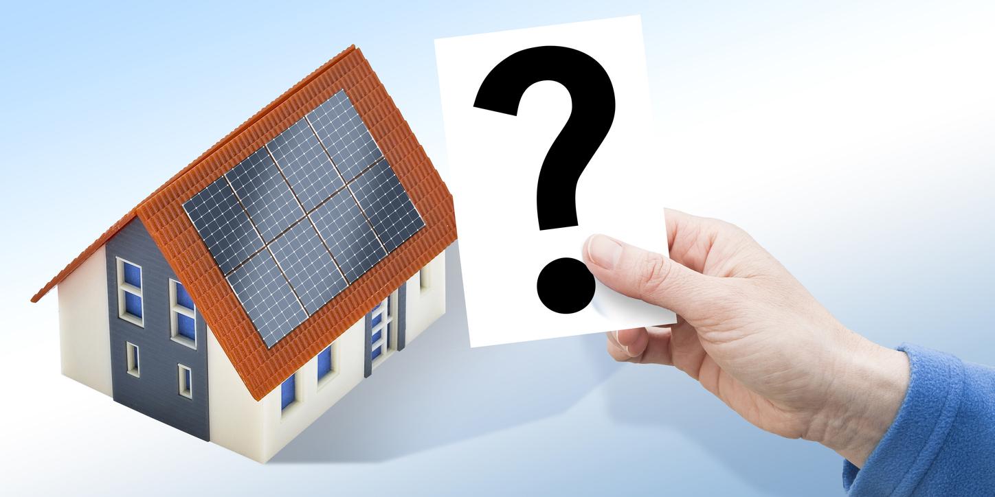 太陽光パネルが屋根に設置された一軒家。右側にはハテナマークが書かれた紙を持っている手