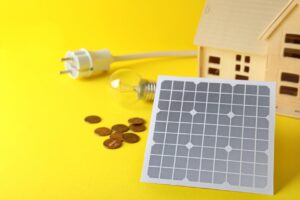 黄色の背景に木の家とコンセント、小銭、ソーラーパネルがあるイラスト