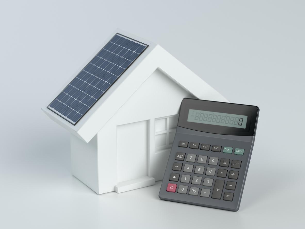 白い背景で太陽光パネルが屋根に設置された白い家、白い家の前に電卓がある画像
