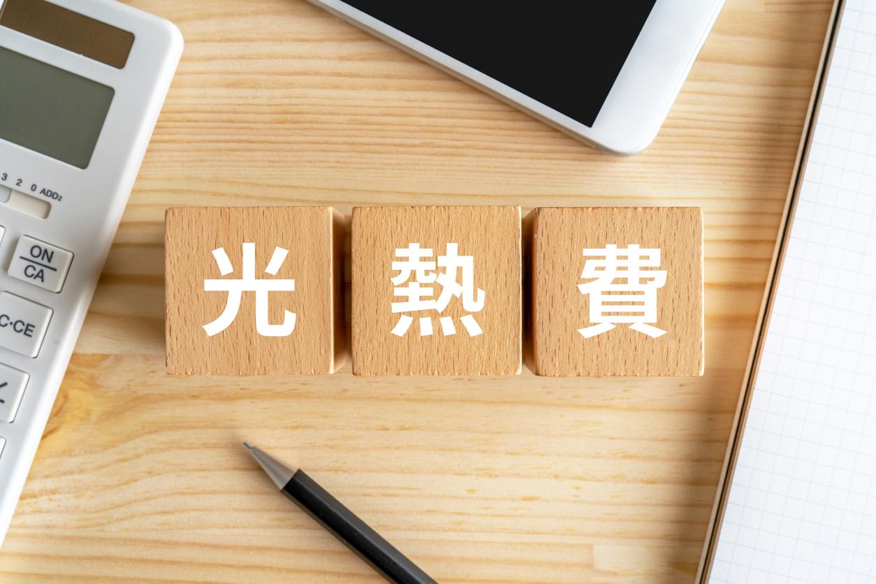 机の上に木のブロックが3つ並べていて「光熱費」と1文字ずつ書かれていて、電卓とスマートフォンとペンとノートで囲まれている画像。