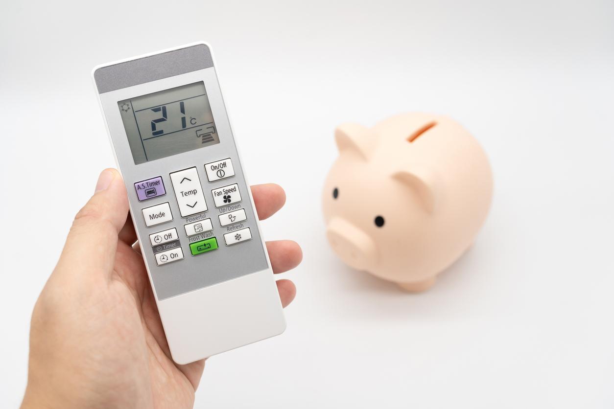エアコンのリモコンを手に持ち、表示は冷房21℃。その隣には豚の貯金箱が置かれている画像
