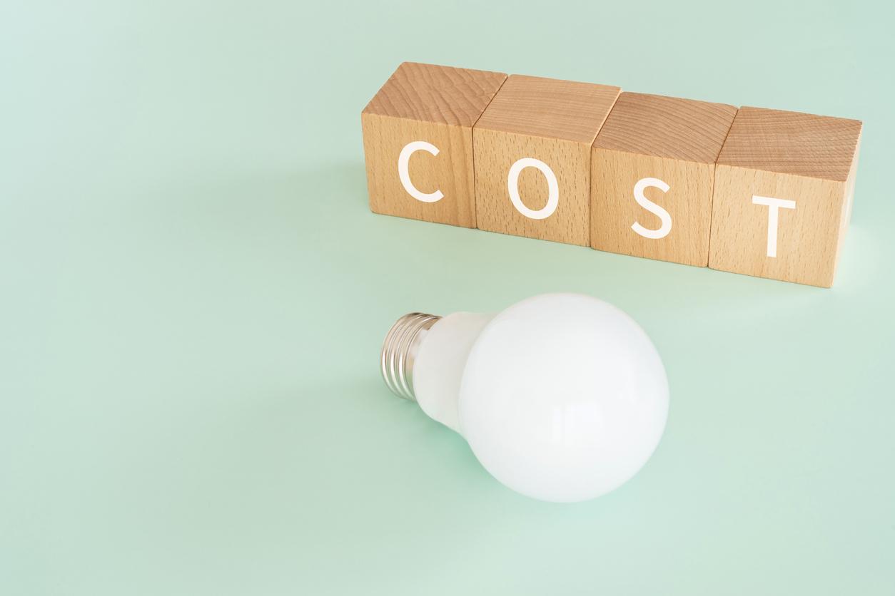 木のブロックが4つ横に並んでいてボックスには1文字づつCOSTと書かれている。ボックスの前には電球がおかれている画像。