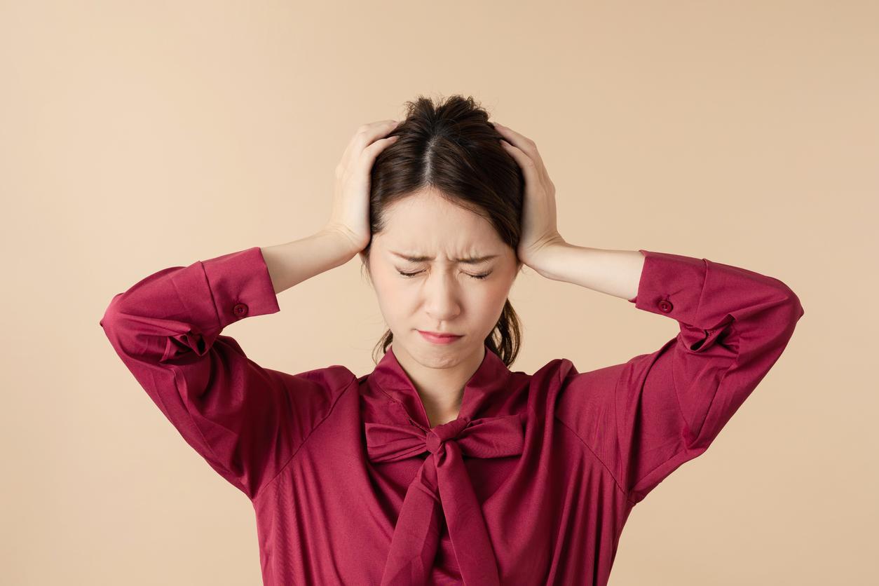 赤いリボンブラウスを着た女性が両手で頭を抱えて悩んでいる画像